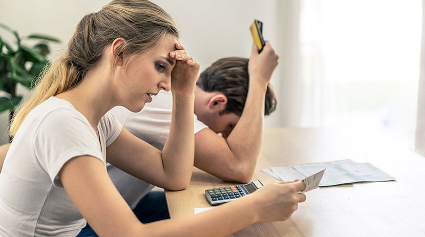 Person using calculator with small house models and laptop on table