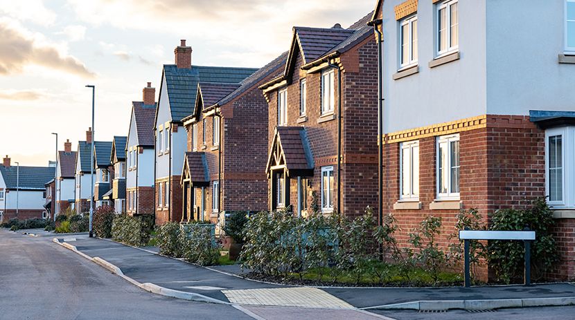 Person using calculator with small house models and laptop on table