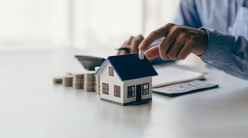 Person using calculator with small house models and laptop on table